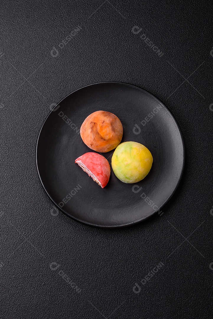 Deliciosos doces mochi asiáticos coloridos com casca de massa de arroz e recheio de frutas em fundo escuro de concreto