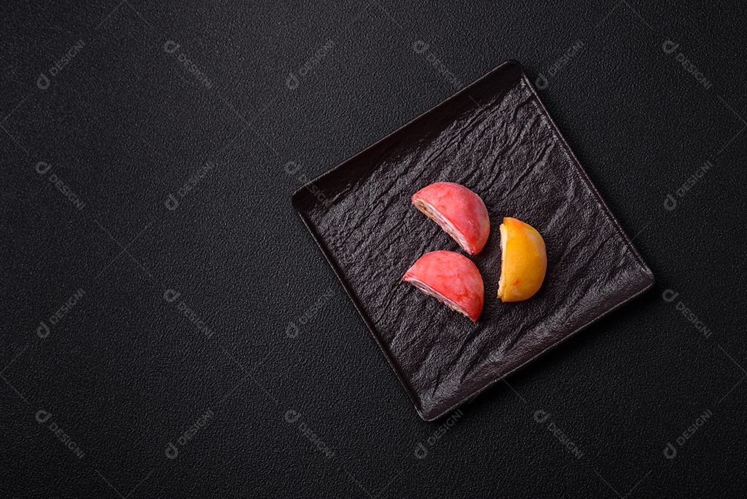 Deliciosos doces mochi asiáticos coloridos com casca de massa de arroz e recheio de frutas em fundo escuro de concreto