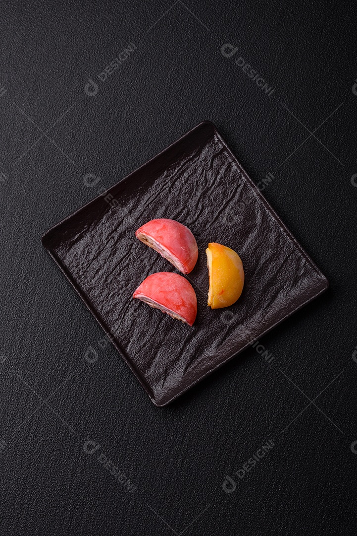 Deliciosos doces mochi asiáticos coloridos com casca de massa de arroz e recheio de frutas em fundo escuro de concreto
