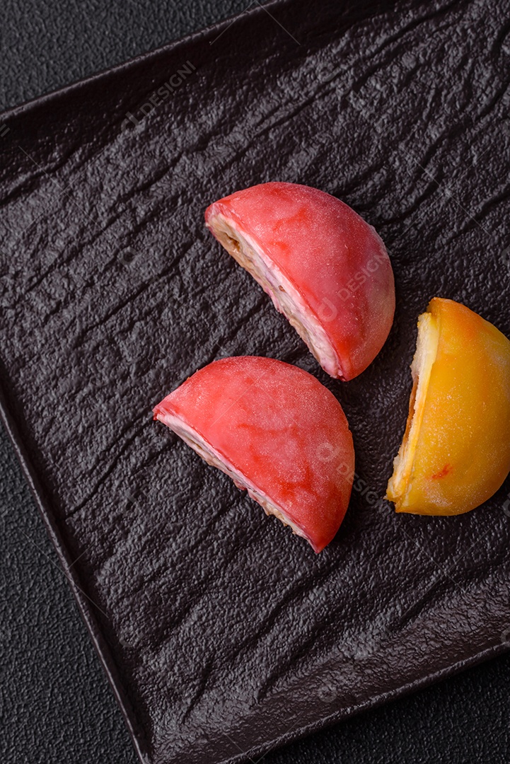 Deliciosos doces mochi asiáticos coloridos com casca de massa de arroz e recheio de frutas em fundo escuro de concreto