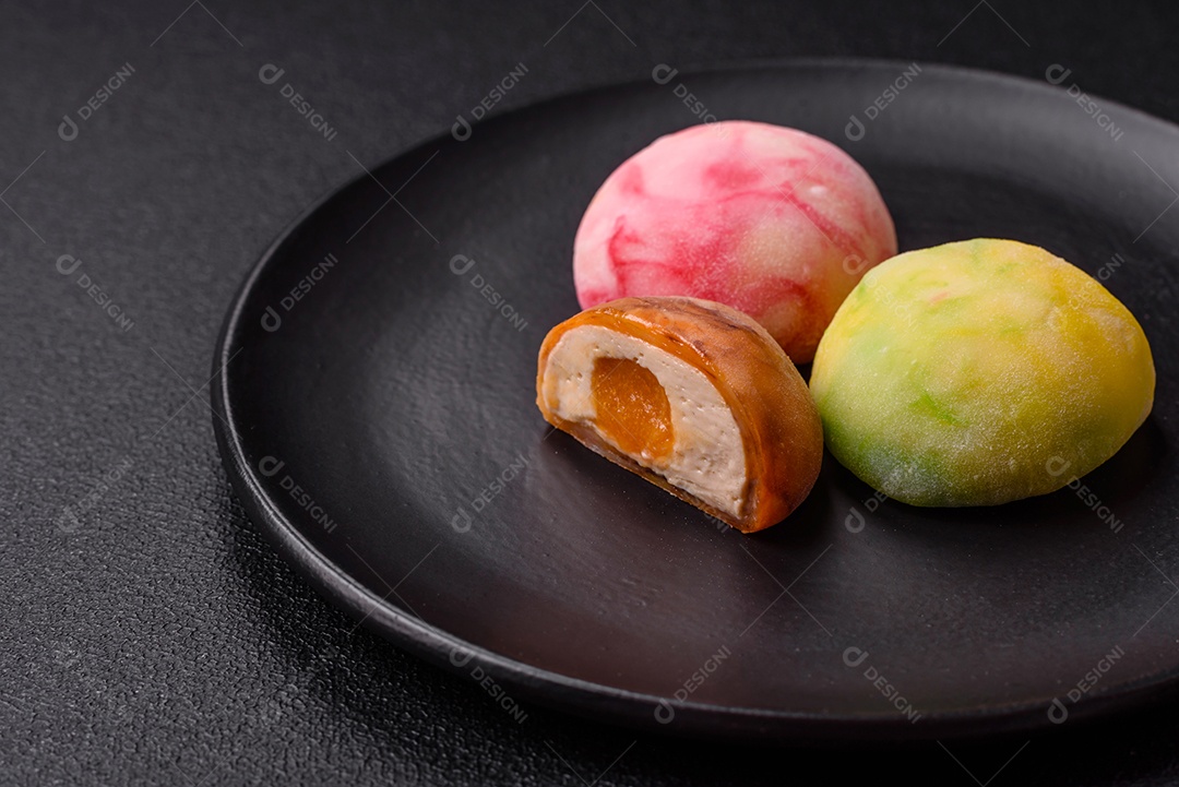Deliciosos doces mochi asiáticos coloridos com casca de massa de arroz e recheio de frutas em fundo escuro de concreto