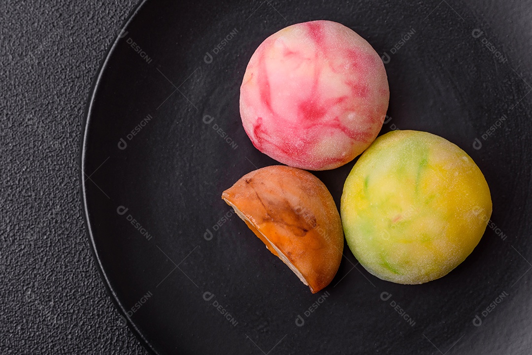 Deliciosos doces mochi asiáticos coloridos com casca de massa de arroz e recheio de frutas em fundo escuro de concreto