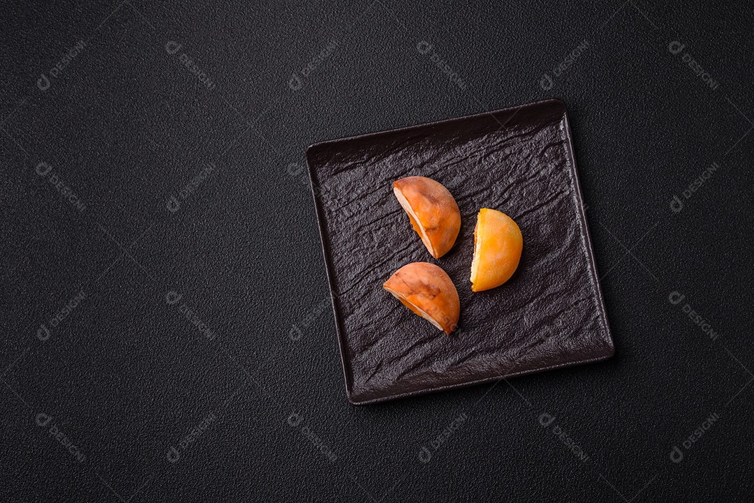 Deliciosos doces mochi asiáticos coloridos com casca de massa de arroz e recheio de frutas em fundo escuro de concreto