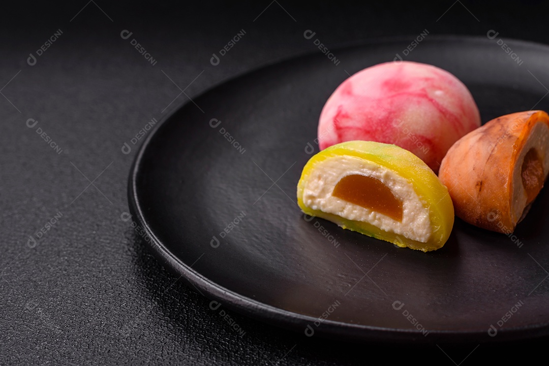 Deliciosos doces mochi asiáticos coloridos com casca de massa de arroz e recheio de frutas em fundo escuro de concreto