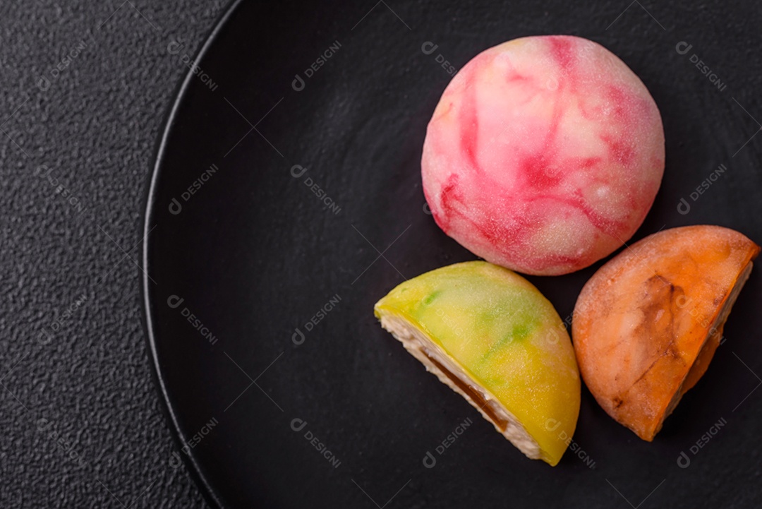 Deliciosos doces mochi asiáticos coloridos com casca de massa de arroz e recheio de frutas em fundo escuro de concreto