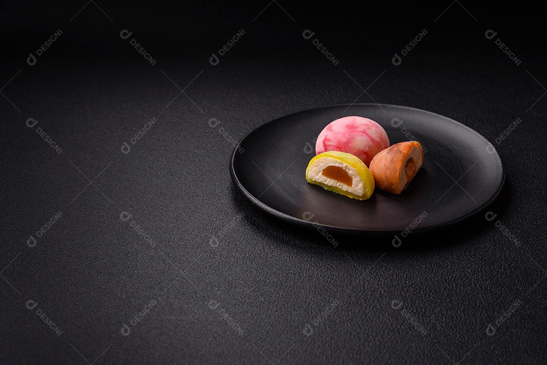 Deliciosos doces mochi asiáticos coloridos com casca de massa de arroz e recheio de frutas em fundo escuro de concreto