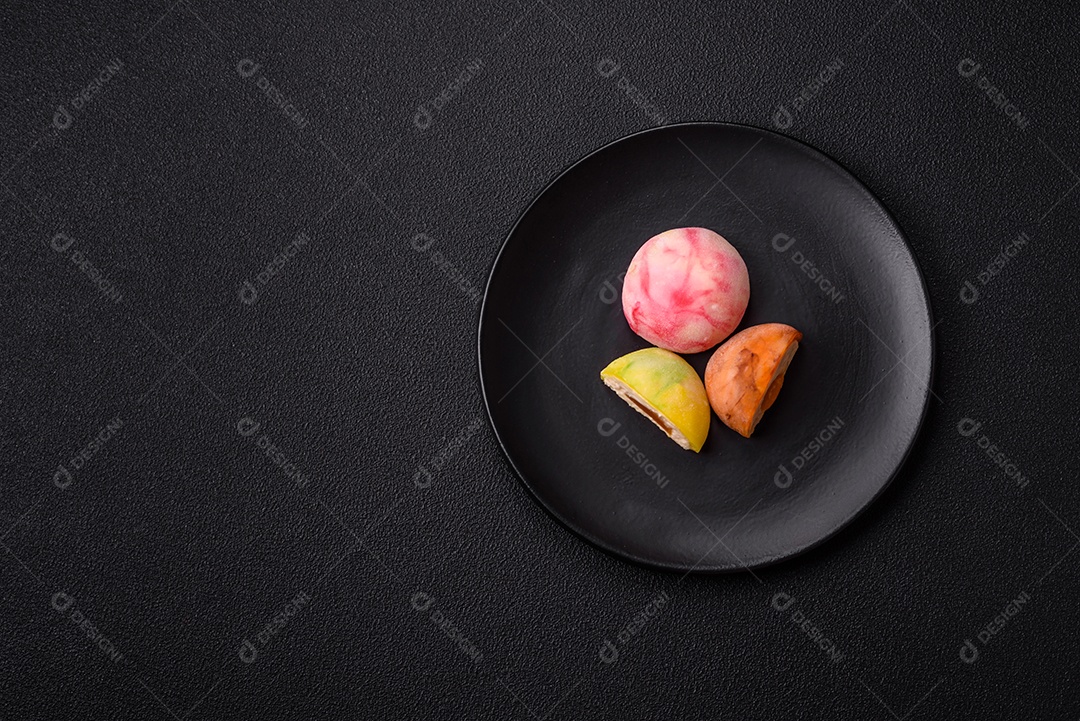 Deliciosos doces mochi asiáticos coloridos com casca de massa de arroz e recheio de frutas em fundo escuro de concreto