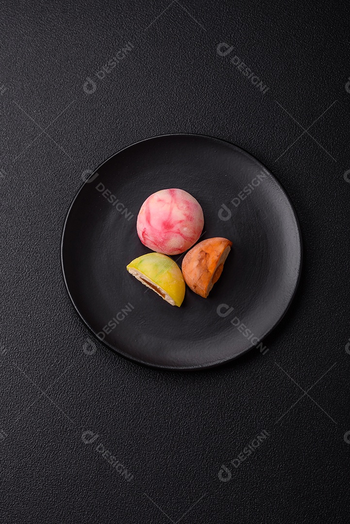 Deliciosos doces mochi asiáticos coloridos com casca de massa de arroz e recheio de frutas em fundo escuro de concreto