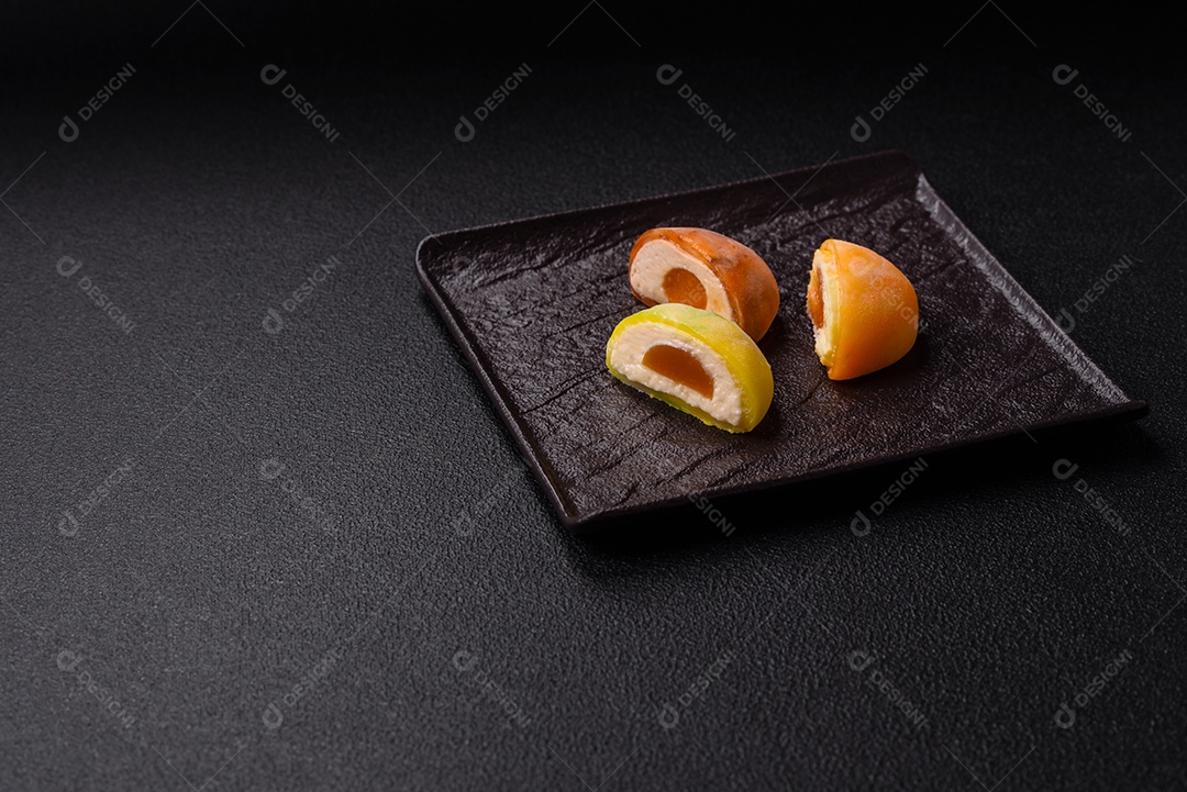 Deliciosos doces mochi asiáticos coloridos com casca de massa de arroz e recheio de frutas em fundo escuro de concreto