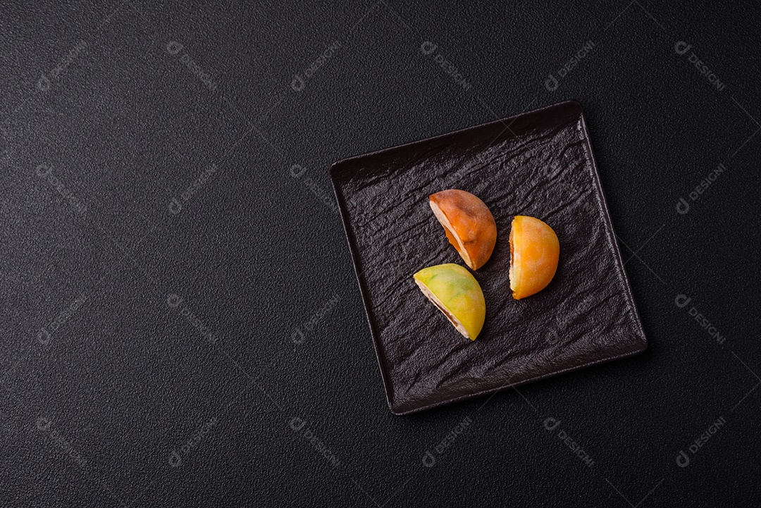 Deliciosos doces mochi asiáticos coloridos com casca de massa de arroz e recheio de frutas em fundo escuro de concreto