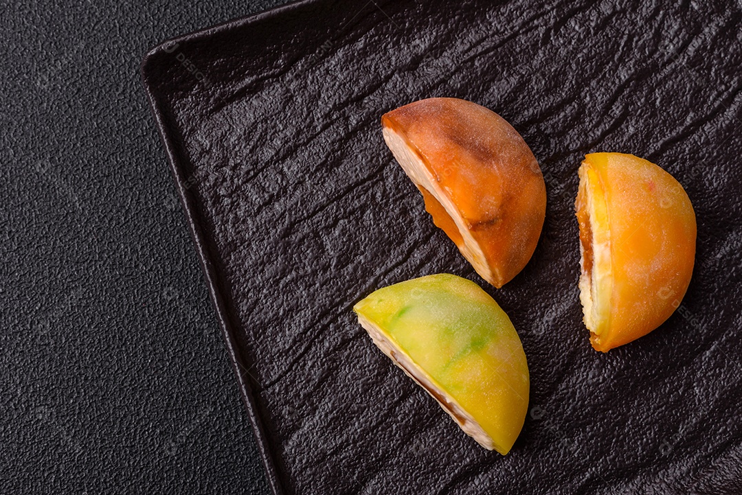 Deliciosos doces mochi asiáticos coloridos com casca de massa de arroz e recheio de frutas em fundo escuro de concreto