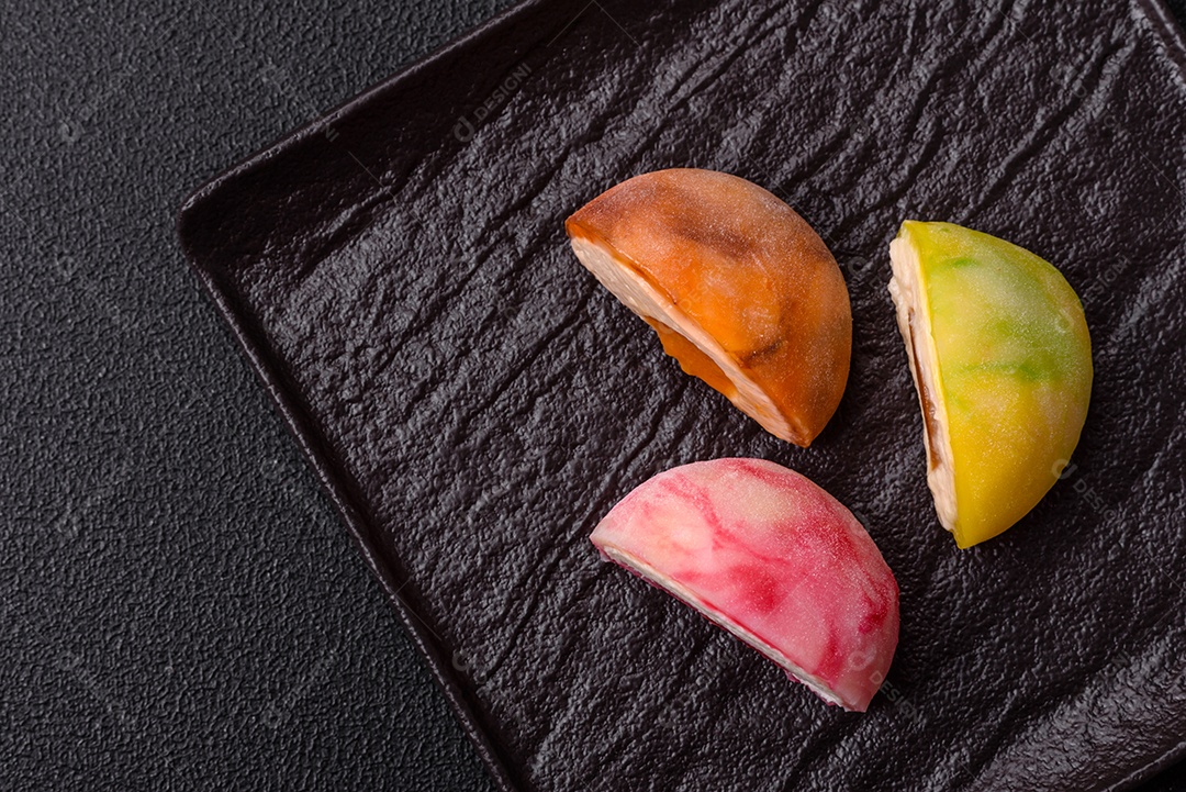Deliciosos doces mochi asiáticos coloridos com casca de massa de arroz e recheio de frutas em fundo escuro de concreto