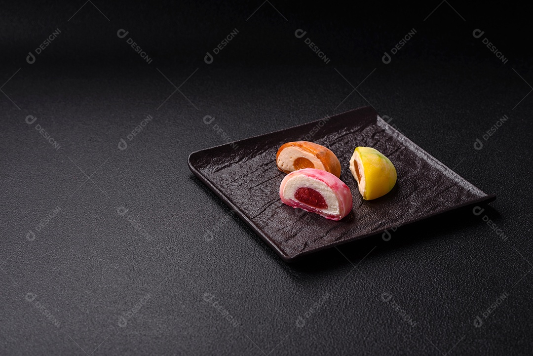Deliciosos doces mochi asiáticos coloridos com casca de massa de arroz e recheio de frutas em fundo escuro de concret