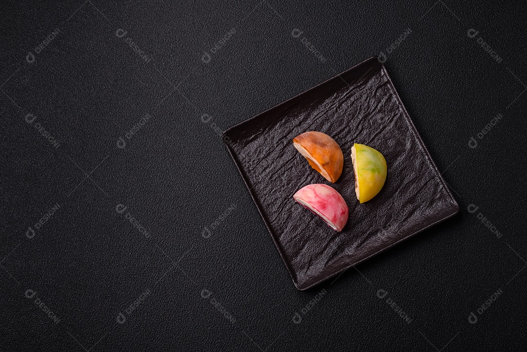 Deliciosos doces mochi asiáticos coloridos com casca de massa de arroz e recheio de frutas em fundo escuro de concreto