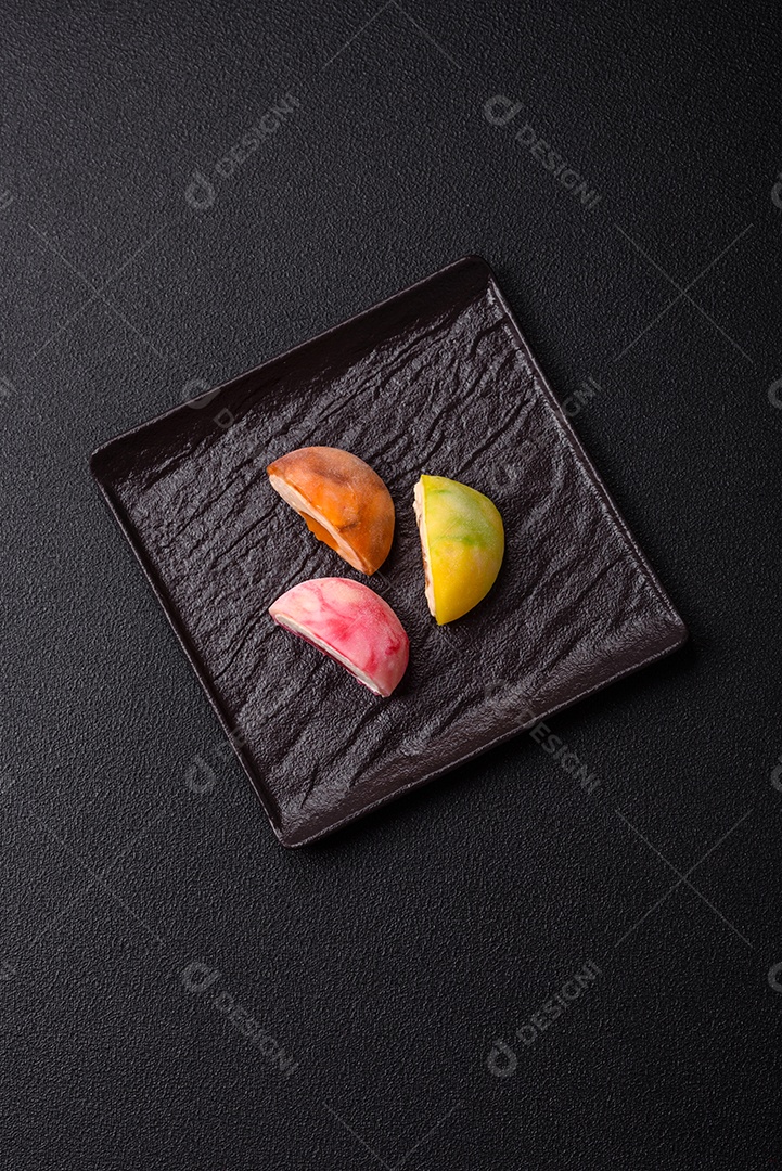 Deliciosos doces mochi asiáticos coloridos com casca de massa de arroz e recheio de frutas em fundo escuro de concreto
