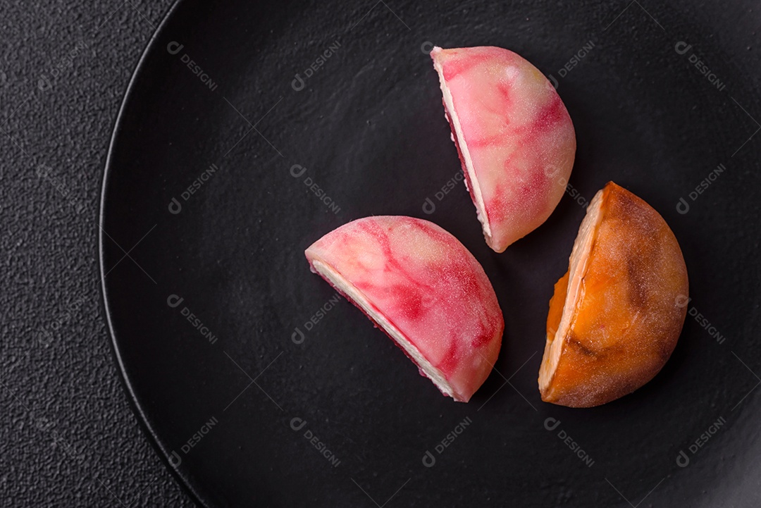 Deliciosos doces mochi asiáticos coloridos com casca de massa de arroz e recheio de frutas em fundo escuro de concreto