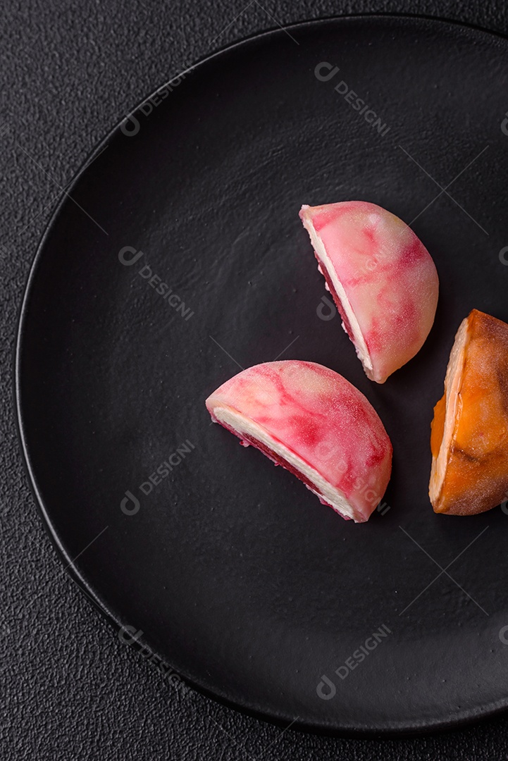 Deliciosos doces mochi asiáticos coloridos com casca de massa de arroz e recheio de frutas em fundo escuro de concreto