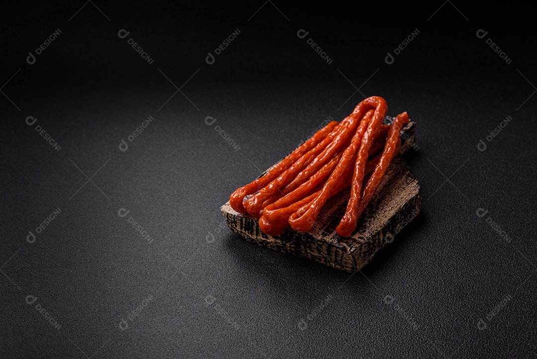 Mini salsichas ou cabanosi defumados com sal e especiarias sobre fundo escuro de concreto
