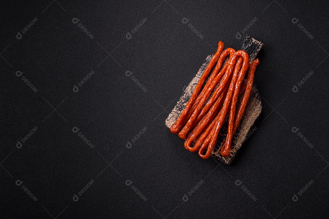 Mini salsichas ou cabanosi defumados com sal e especiarias sobre fundo escuro de concreto