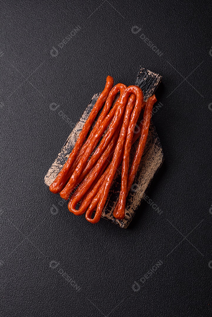 Mini salsichas ou cabanosi defumados com sal e especiarias sobre fundo escuro de concreto