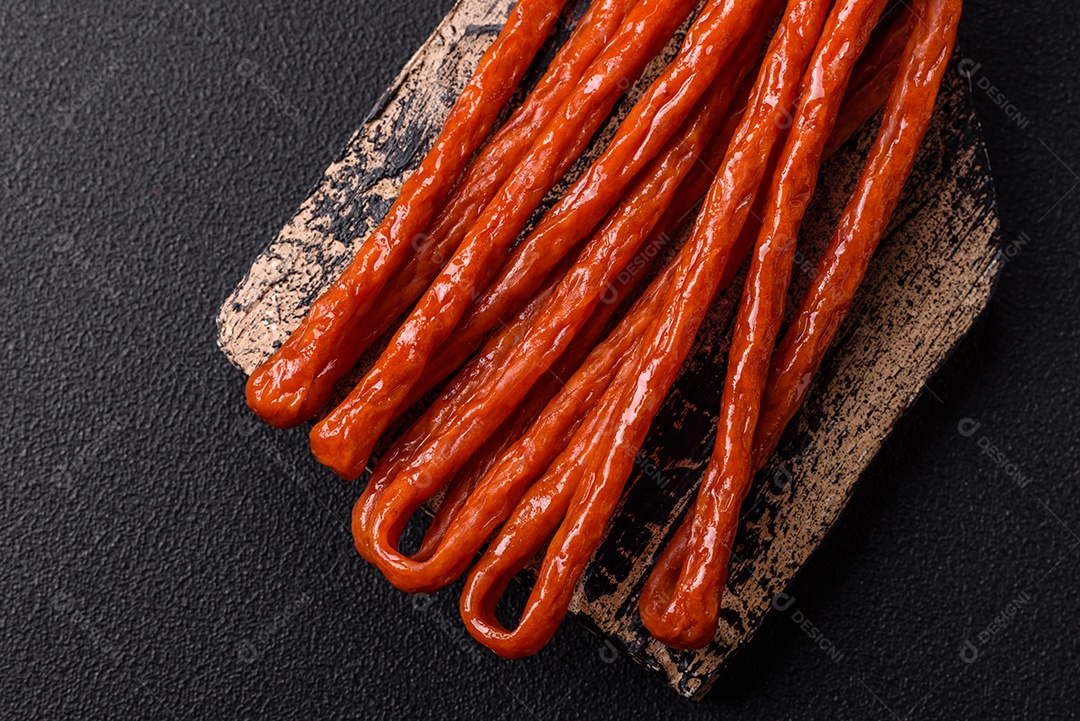 Mini salsichas ou cabanosi defumados com sal e especiarias sobre fundo escuro de concreto