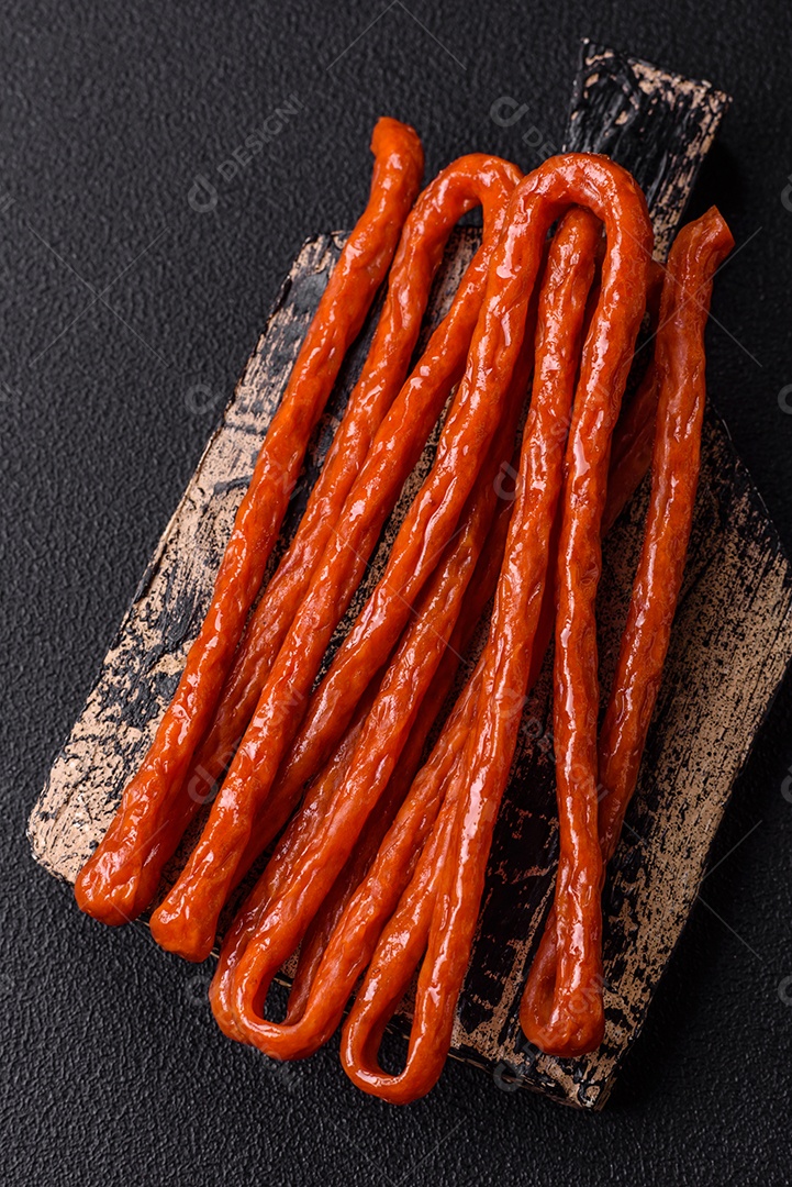 Mini salsichas ou cabanosi defumados com sal e especiarias sobre fundo escuro de concreto