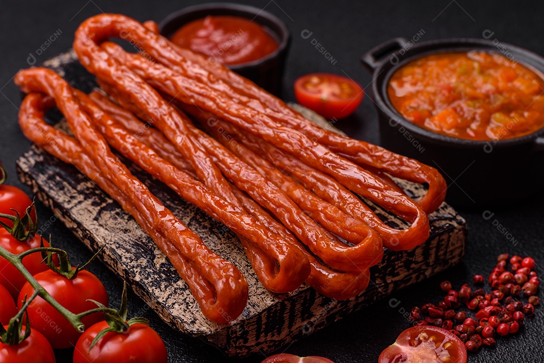 Mini salsichas ou cabanosi defumados com sal e especiarias sobre fundo escuro de concreto