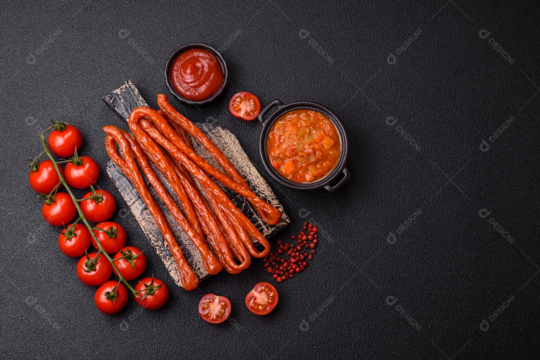 Mini salsichas ou cabanosi defumados com sal e especiarias sobre fundo escuro de concreto