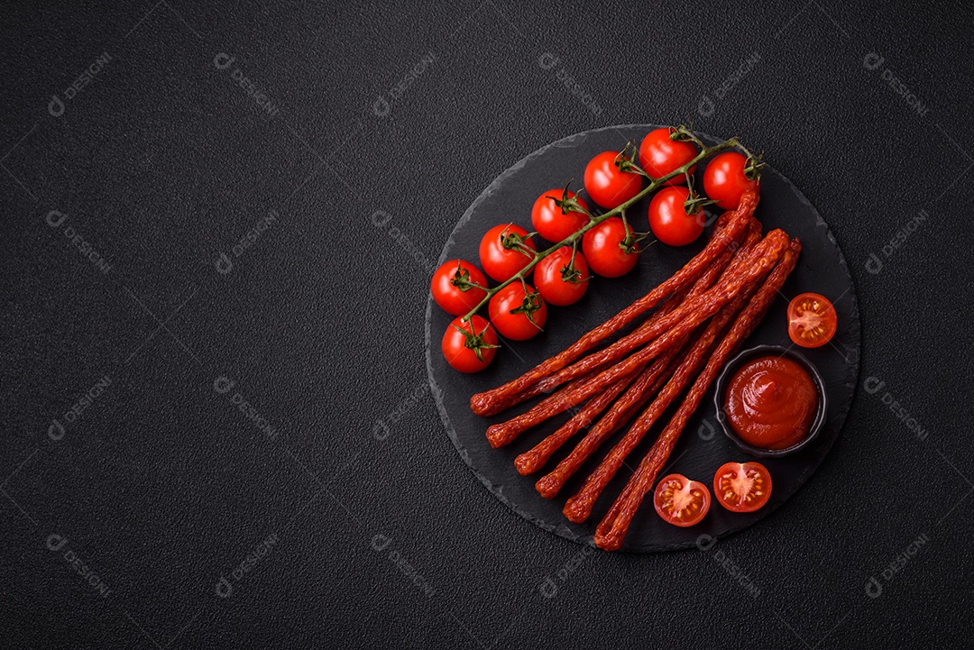 Mini salsichas ou cabanosi defumados com sal e especiarias sobre fundo escuro de concret