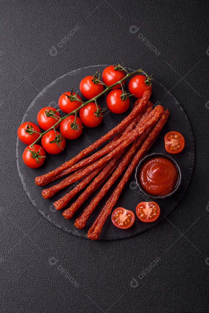 Mini salsichas ou cabanosi defumados com sal e especiarias sobre fundo escuro de concreto