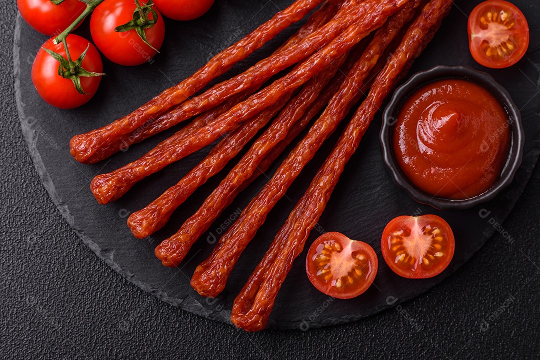 Mini salsichas ou cabanosi defumados com sal e especiarias sobre fundo escuro de concreto