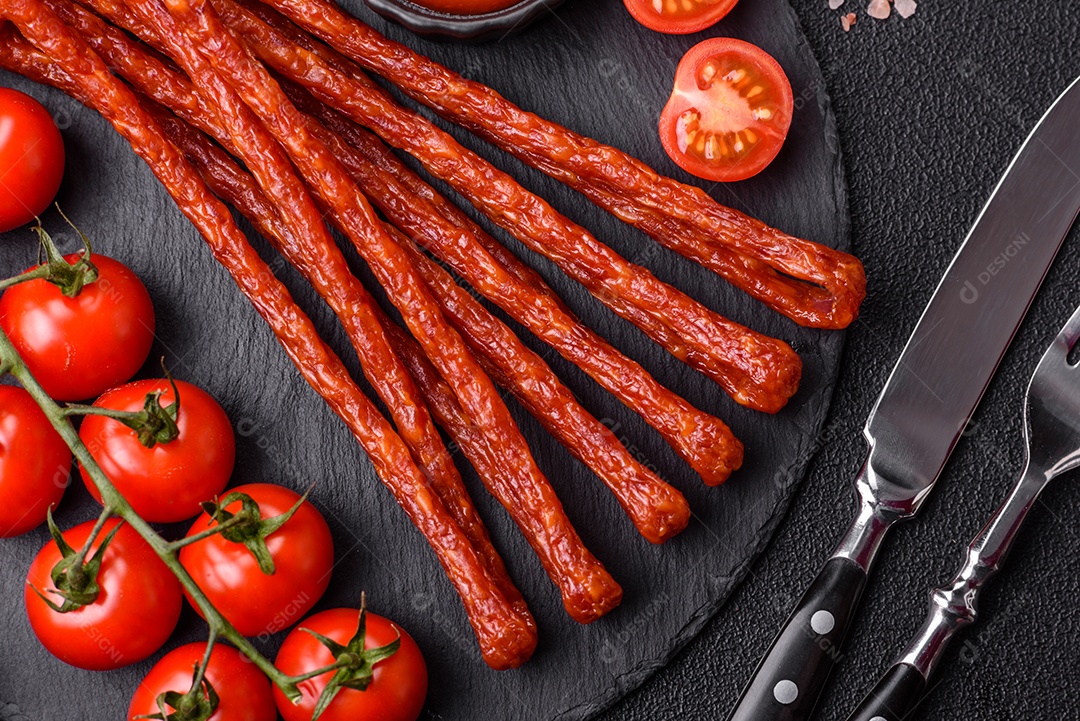 Mini salsichas ou cabanosi defumados com sal e especiarias sobre fundo escuro de concreto