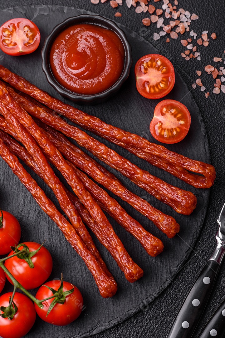 Mini salsichas ou cabanosi defumados com sal e especiarias sobre fundo escuro de concreto