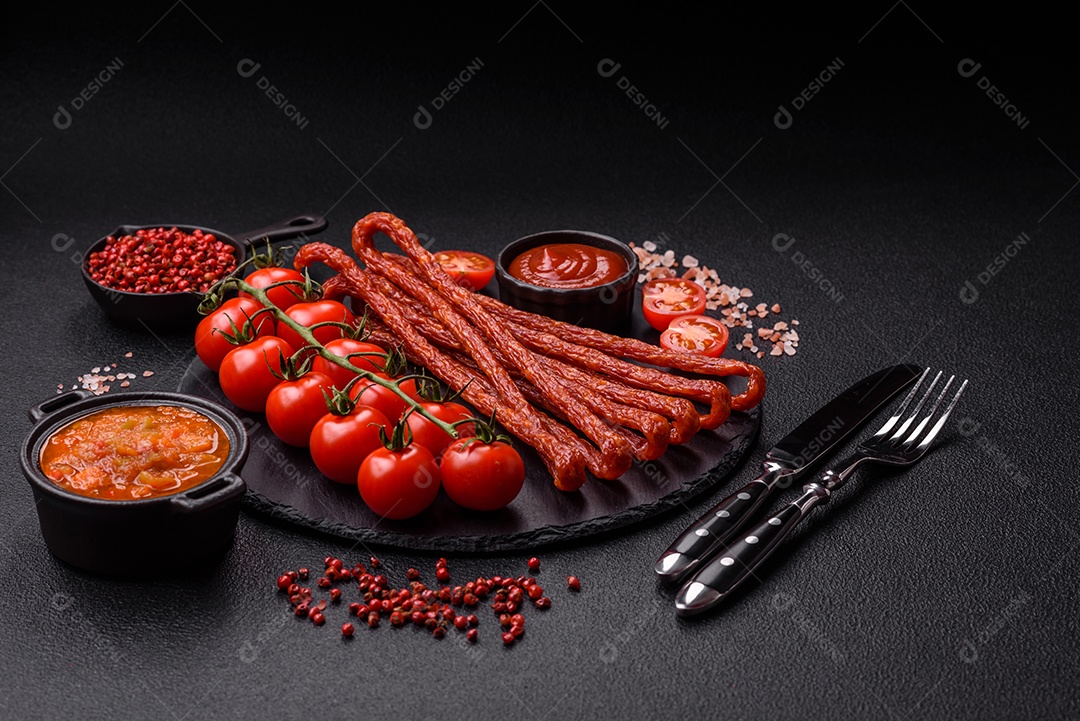 Mini salsichas ou cabanosi defumados com sal e especiarias sobre fundo escuro de concreto