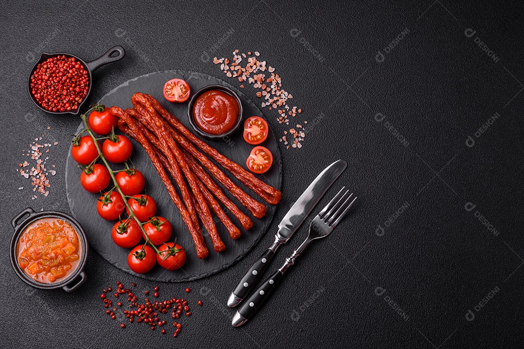 Mini salsichas ou cabanosi defumados com sal e especiarias sobre fundo escuro de concreto