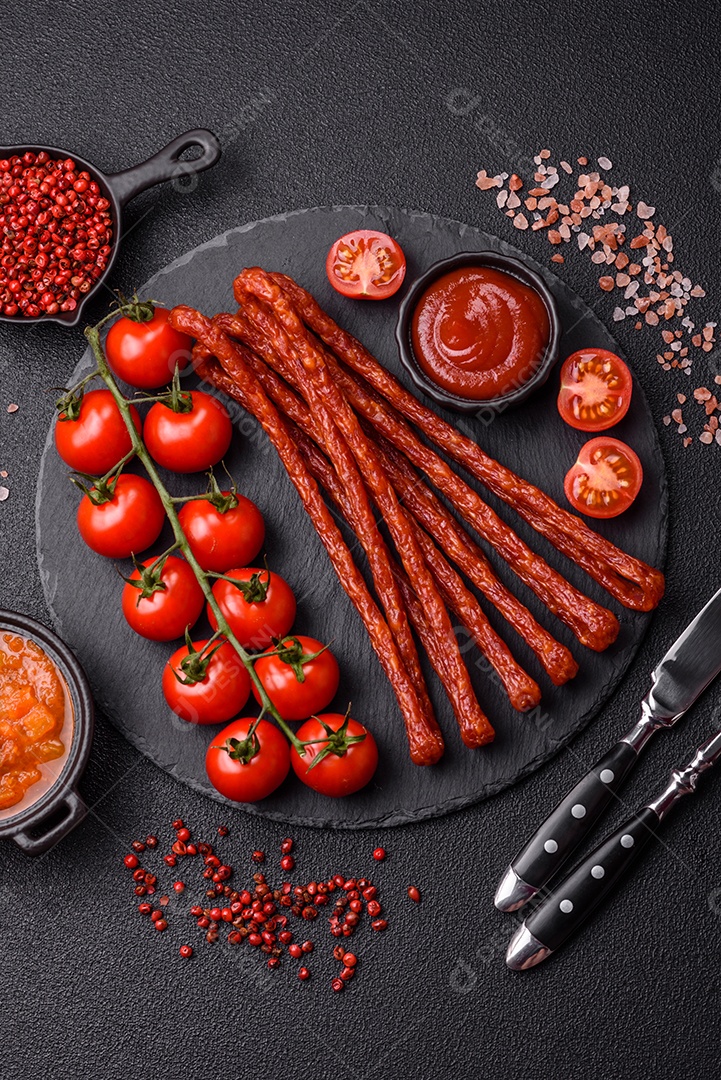 Mini salsichas ou cabanosi defumados com sal e especiarias sobre fundo escuro de concreto