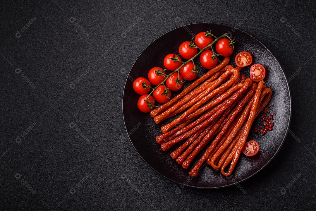 Mini salsichas ou cabanosi defumados com sal e especiarias sobre fundo escuro de concreto