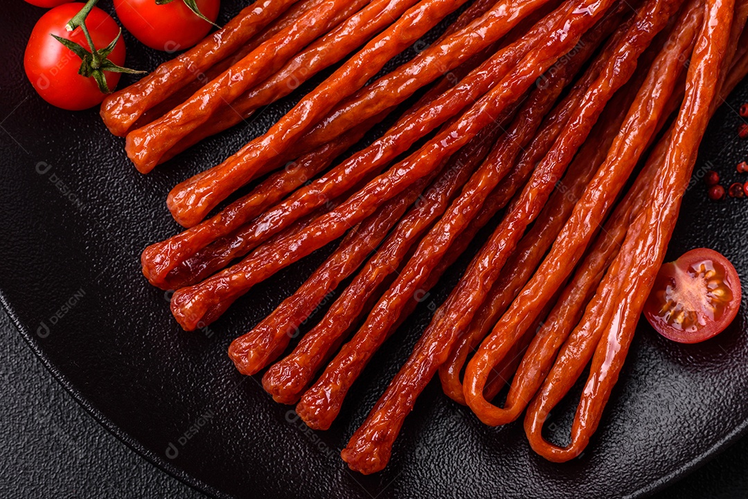 Mini salsichas ou cabanosi defumados com sal e especiarias sobre fundo escuro de concreto