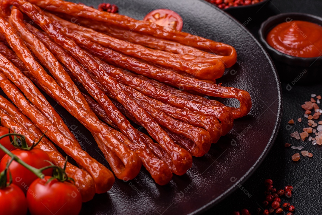 Mini salsichas ou cabanosi defumados com sal e especiarias sobre fundo escuro de concreto