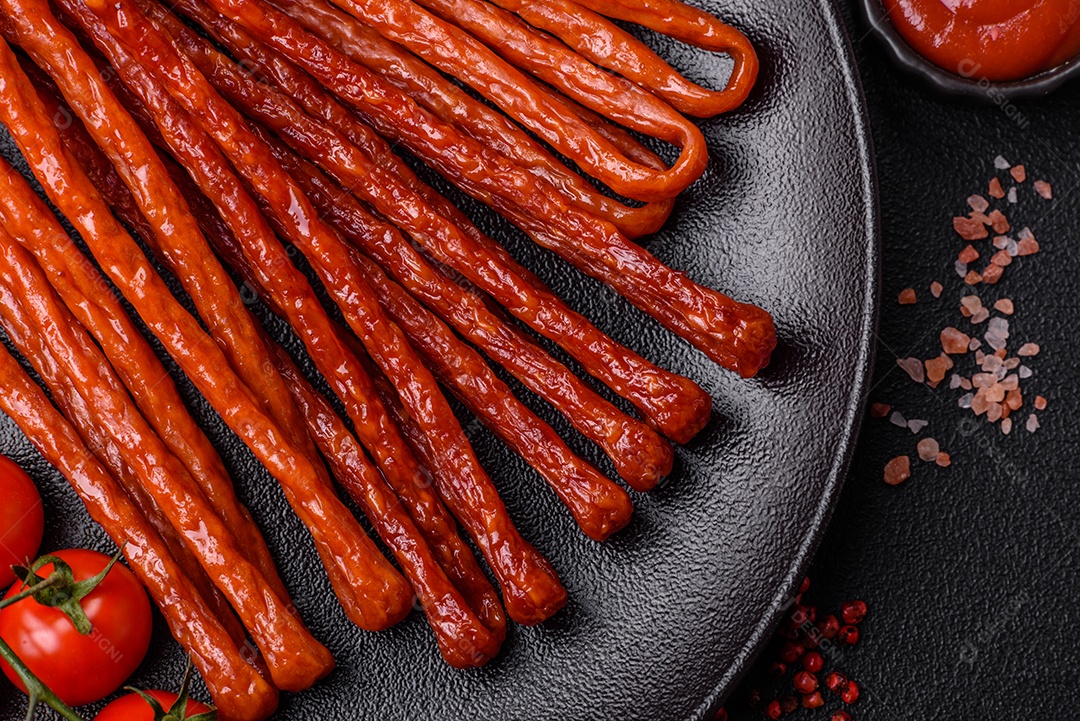 Mini salsichas ou cabanosi defumados com sal e especiarias sobre fundo escuro de concreto