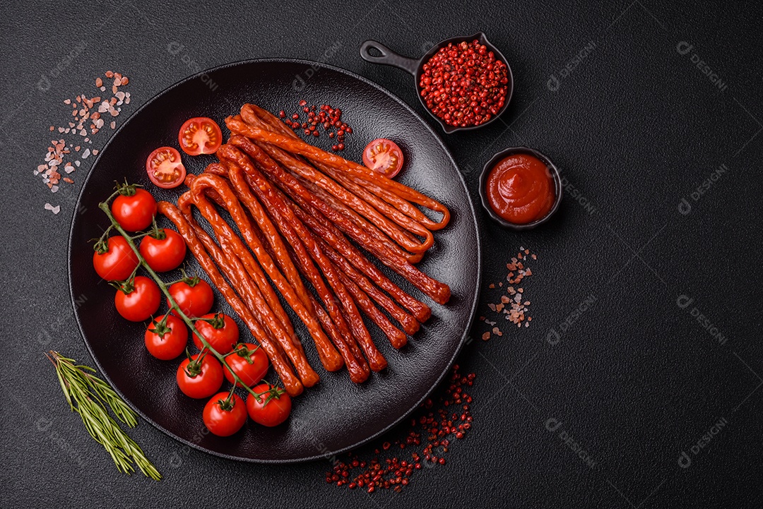 Mini salsichas ou cabanosi defumados com sal e especiarias sobre fundo escuro de concreto