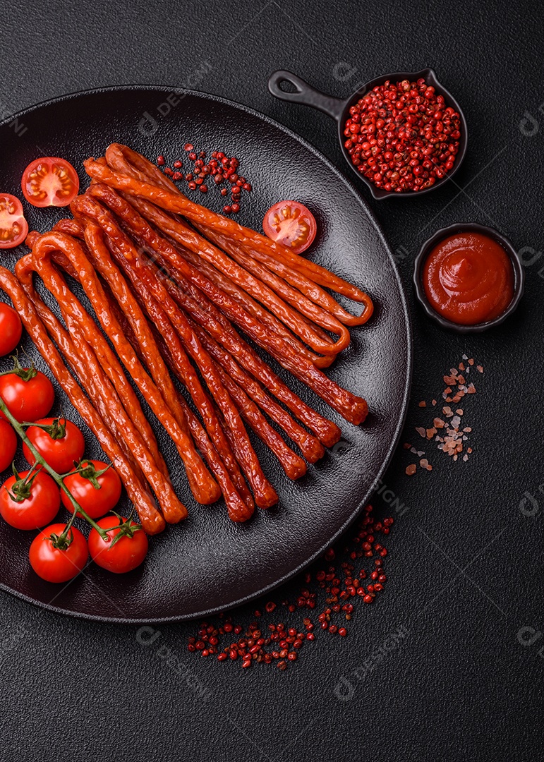 Mini salsichas ou cabanosi defumados com sal e especiarias sobre fundo escuro de concreto