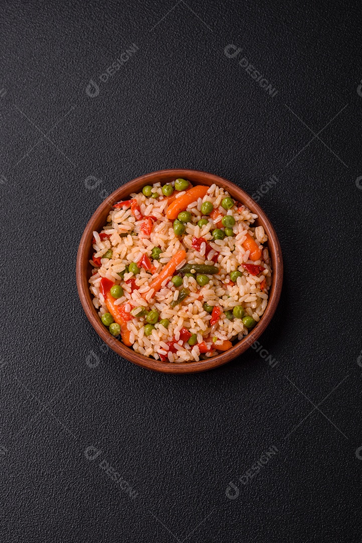 Delicioso arroz cozido com legumes cenouras, ervilhas e pimentões com sal e especiarias sobre um fundo escuro de concreto