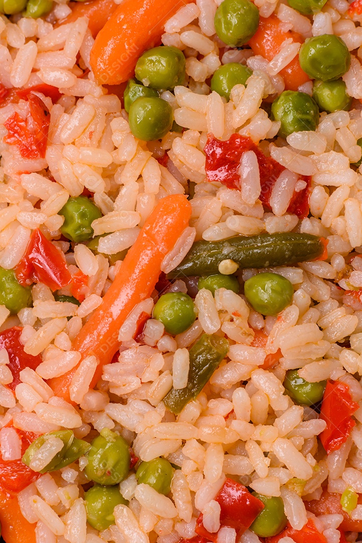 Delicioso arroz cozido com legumes cenouras, ervilhas e pimentões com sal e especiarias sobre um fundo escuro de concreto