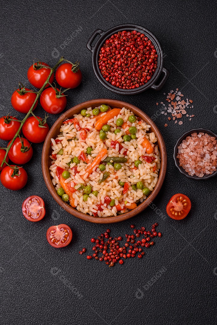 Delicioso arroz cozido com legumes cenouras, ervilhas e pimentões com sal e especiarias sobre um fundo escuro de concreto