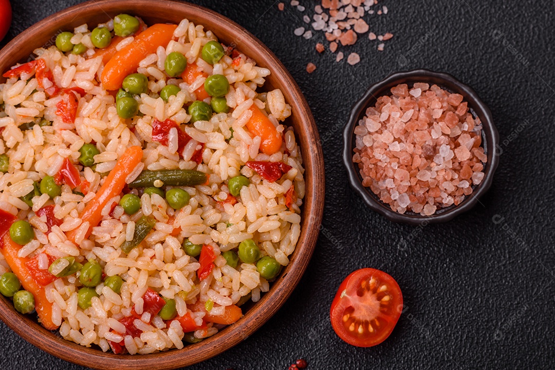 Delicioso arroz cozido com legumes cenouras, ervilhas e pimentões com sal e especiarias sobre um fundo escuro de concreto
