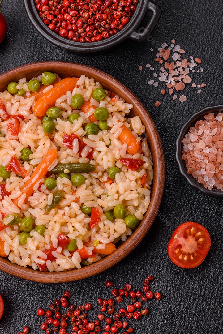 Delicioso arroz cozido com legumes cenouras, ervilhas e pimentões com sal e especiarias sobre um fundo escuro de concreto