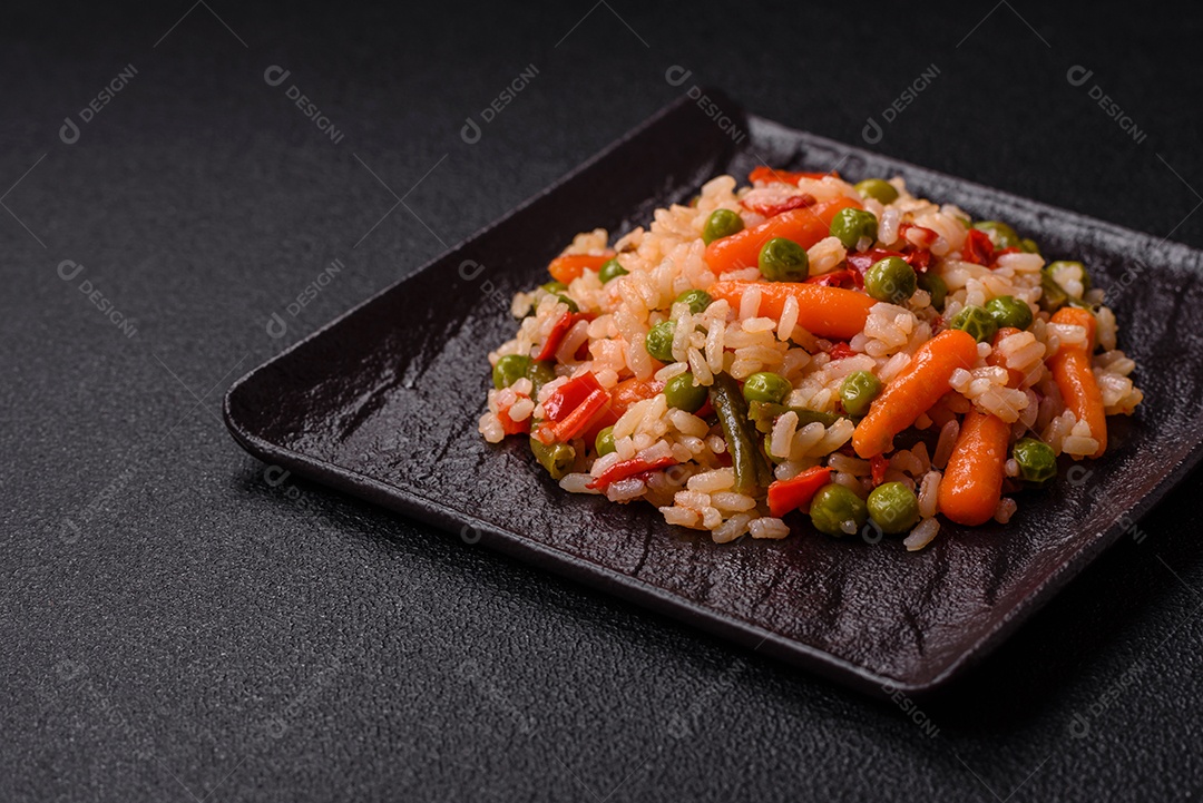 Delicioso arroz cozido com legumes cenouras, ervilhas e pimentões com sal e especiarias sobre um fundo escuro de concreto