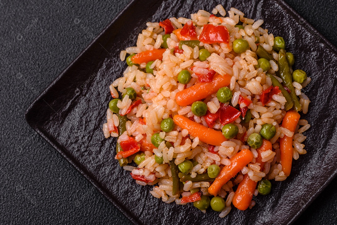 Delicioso arroz cozido com legumes cenouras, ervilhas e pimentões com sal e especiarias sobre um fundo escuro de concreto