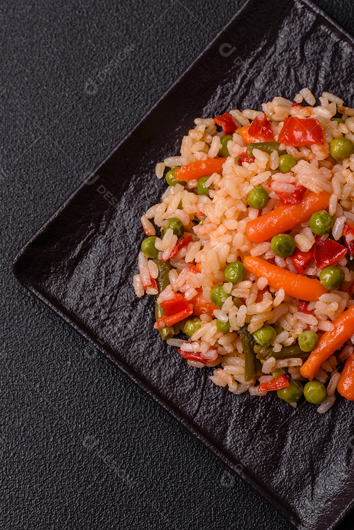 Delicioso arroz cozido com legumes cenouras, ervilhas e pimentões com sal e especiarias sobre um fundo escuro de concreto